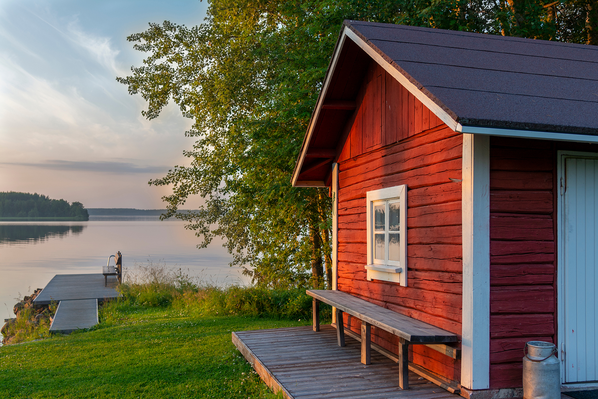 Mökkimaisema, jossa sauna on etualalla ja taustalla näkyy järvi.