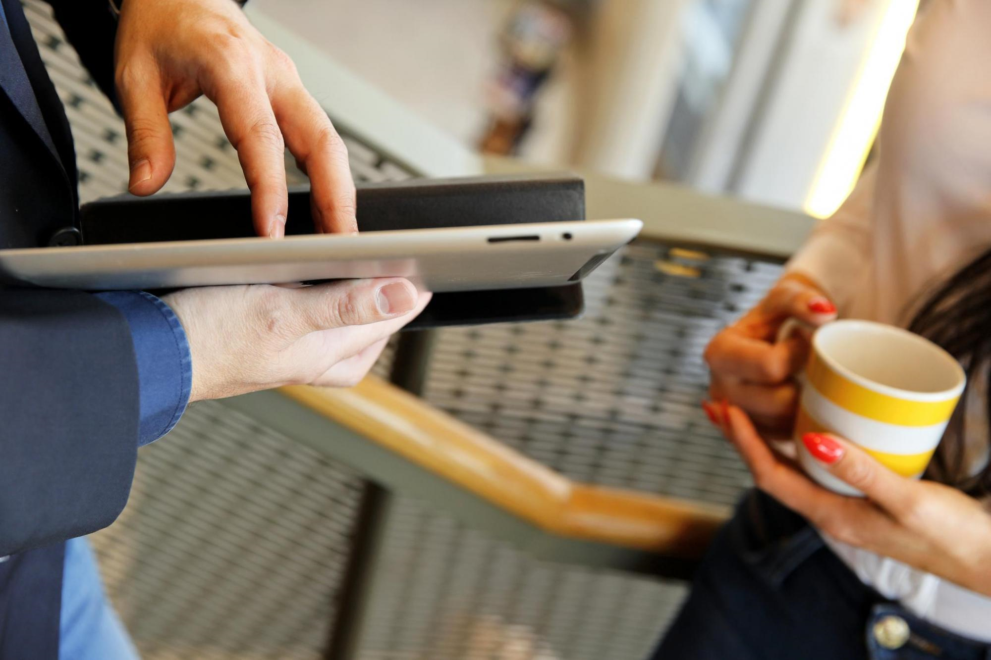 Kahden henkilön kädet, joista toisella läppäri ja toisella kahvikuppi