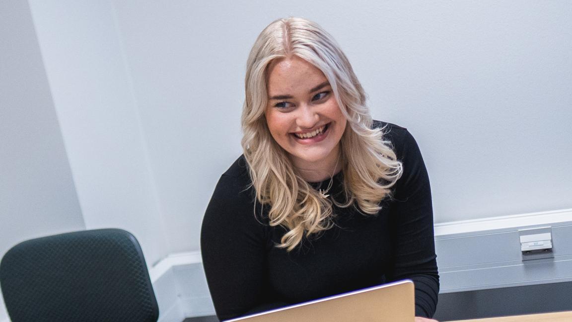 Vaaleatukkainen tyttö hymyilee läppärin ääressä