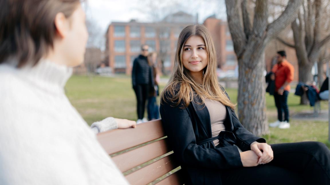 Kaksi opiskelijaa istuu puistonpenkillä