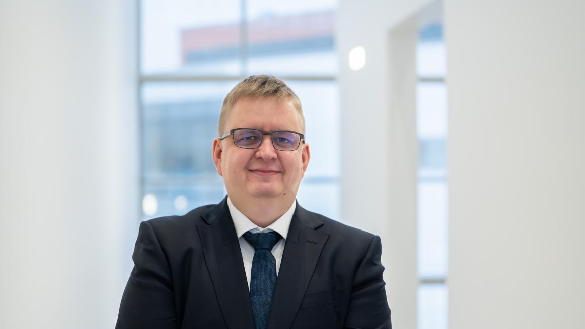 Timo Alho Vaasan yliopistolla, päällä tumma puvuntakki ja kaulassa solmio, katsoo kameraan ja hymyilee tyytyväisenä