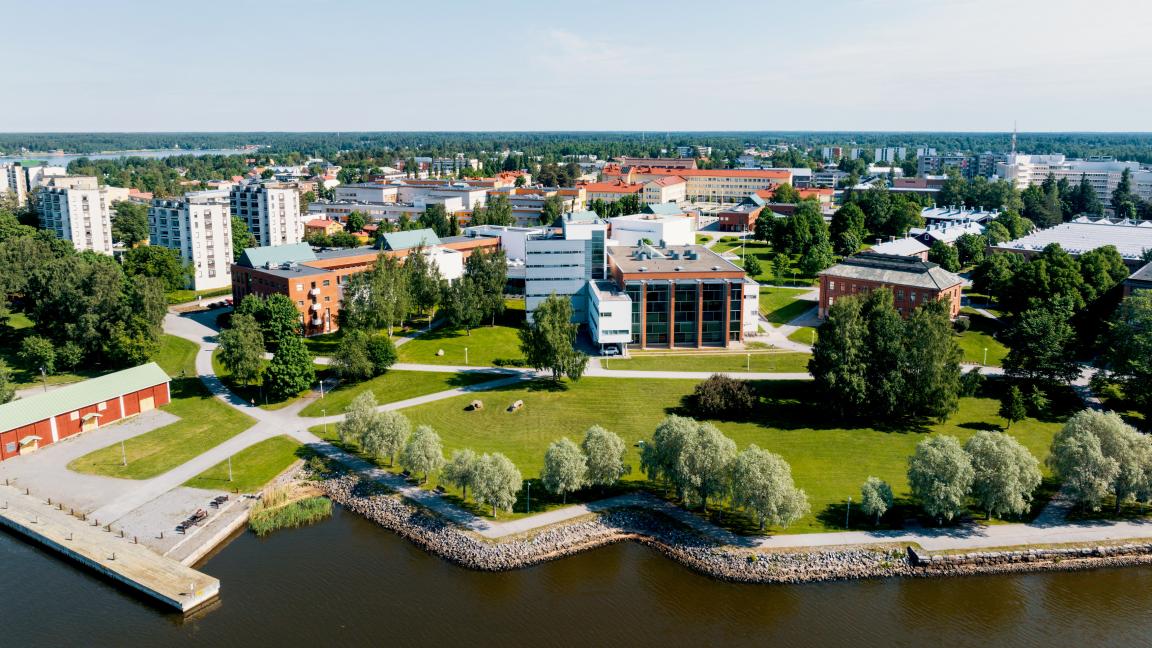 Ilmakuva Vaasan yliopiston kampuksesta. Kuvassa näkyy sininen melkein pilvetön taivas, merta ja yliopiston rakennuksia. Taustalla kaukana näkyy Vaasan kaupunkia.