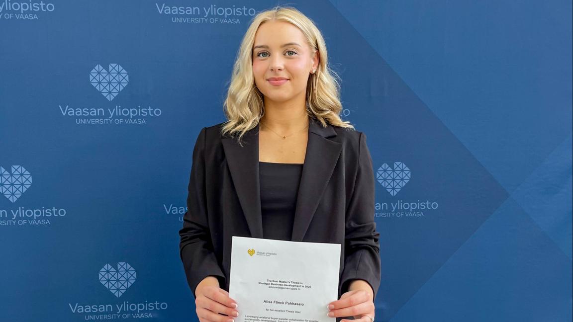 Alisa Flinck Pahkasalo seisomassa yliopiston logoseinän edessä