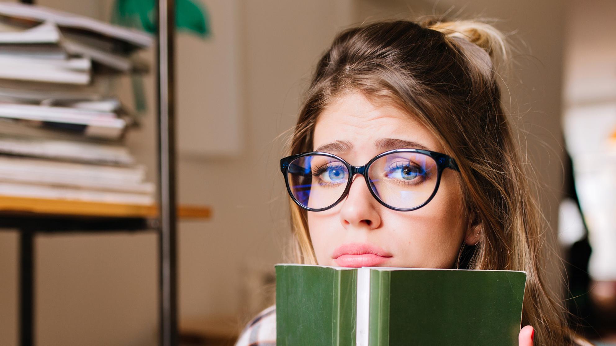 nuori nainen nojaa leukaa kirjaan ja näyttää surulliselta