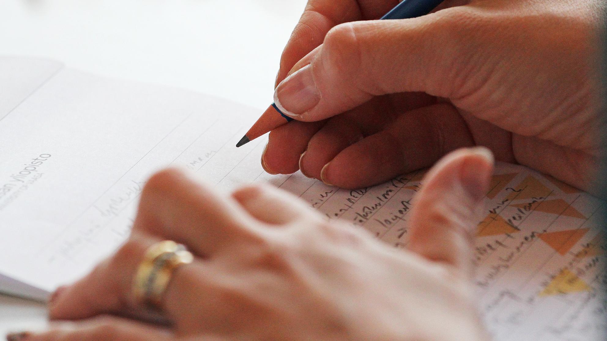 Henkilö kirjoittaa Vaasan yliopiston vihkoon lyijykynällä