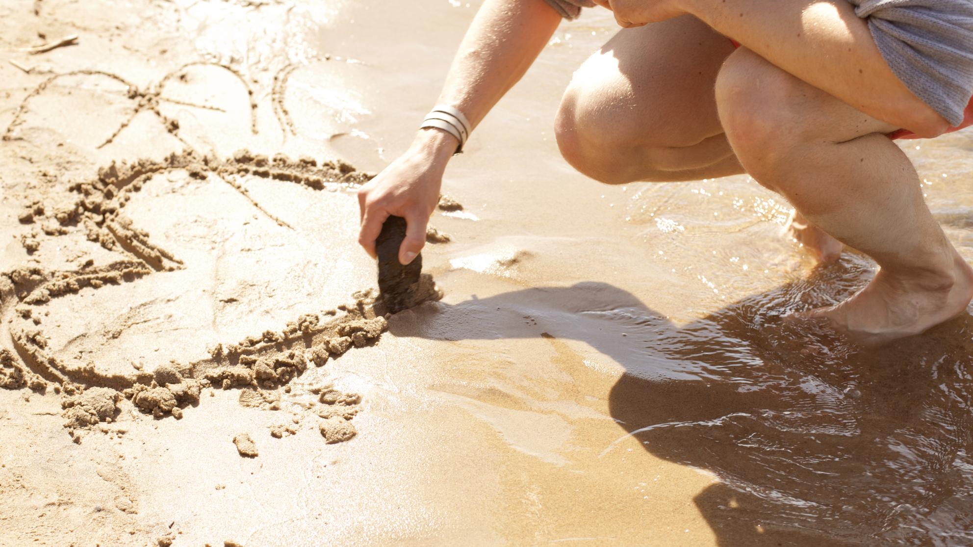 Henkilö piirtää hiekkaan sydämen. 