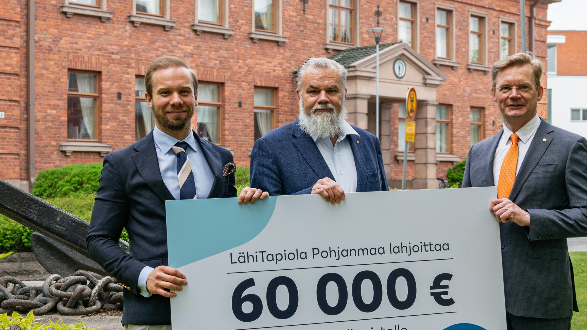 Kuva Joel Sunabackasta, Harry Linnarinteestä ja Jari Kuusistosta Konttorin edessä. He pitelevät 60000 euron lahjoituskylttiä käsissään.