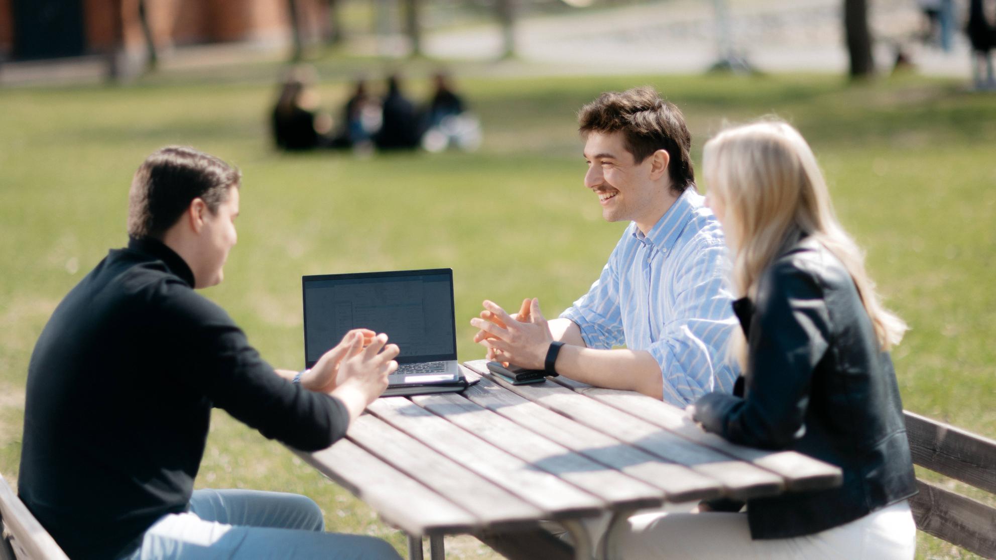 Kolme opiskelijaa keskustelee pöydän ääressä