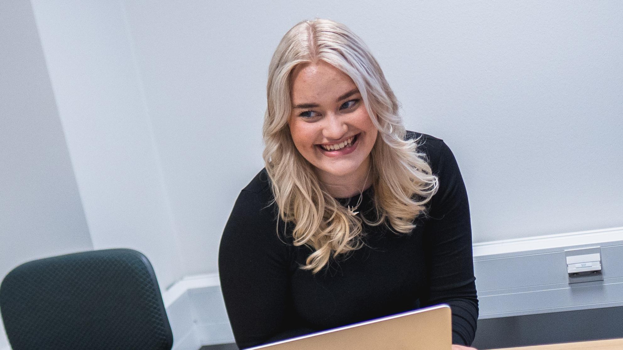 Vaaleatukkainen tyttö hymyilee läppärin ääressä