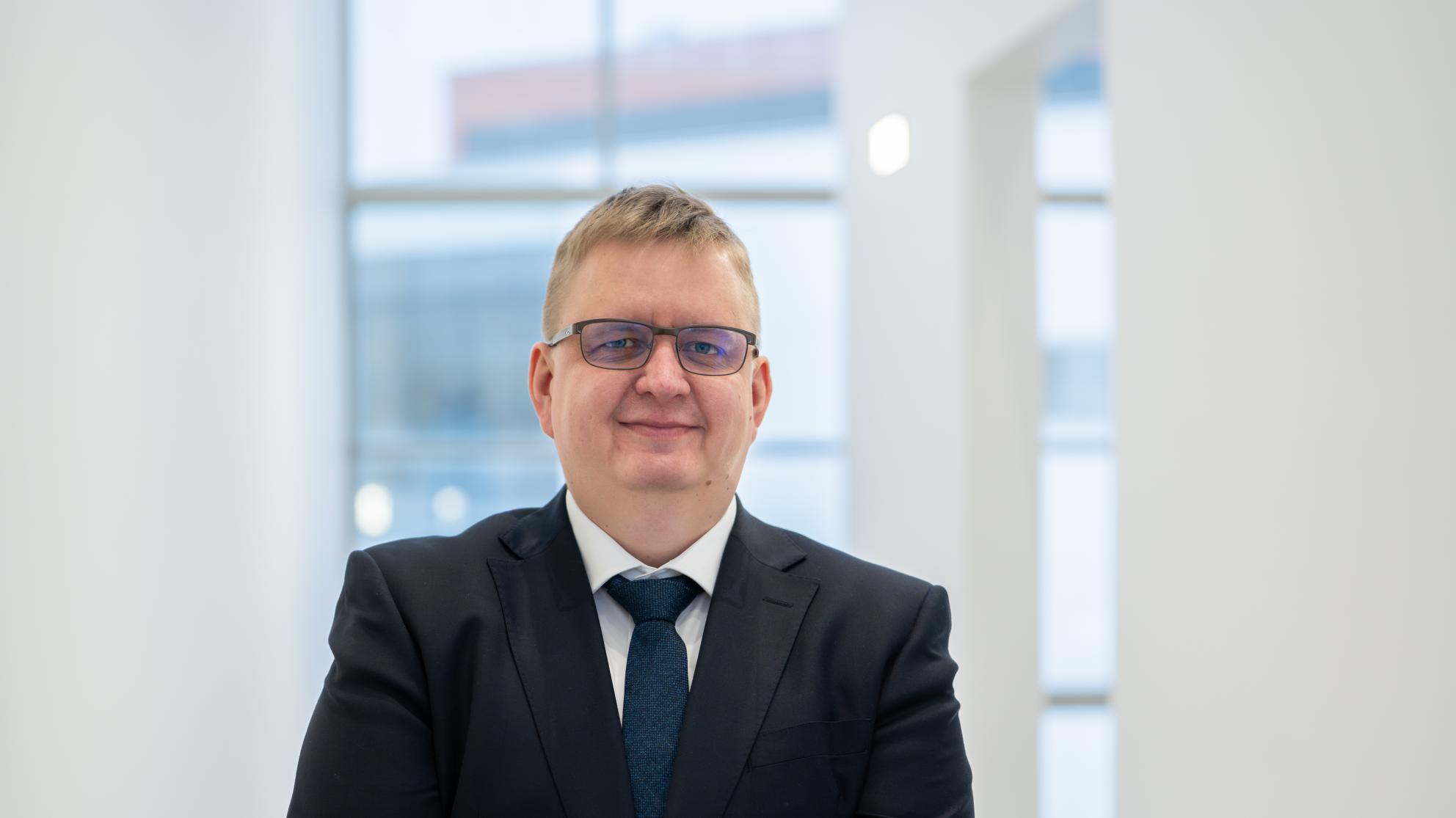 Timo Alho Vaasan yliopistolla, päällä tumma puvuntakki ja kaulassa solmio, katsoo kameraan ja hymyilee tyytyväisenä