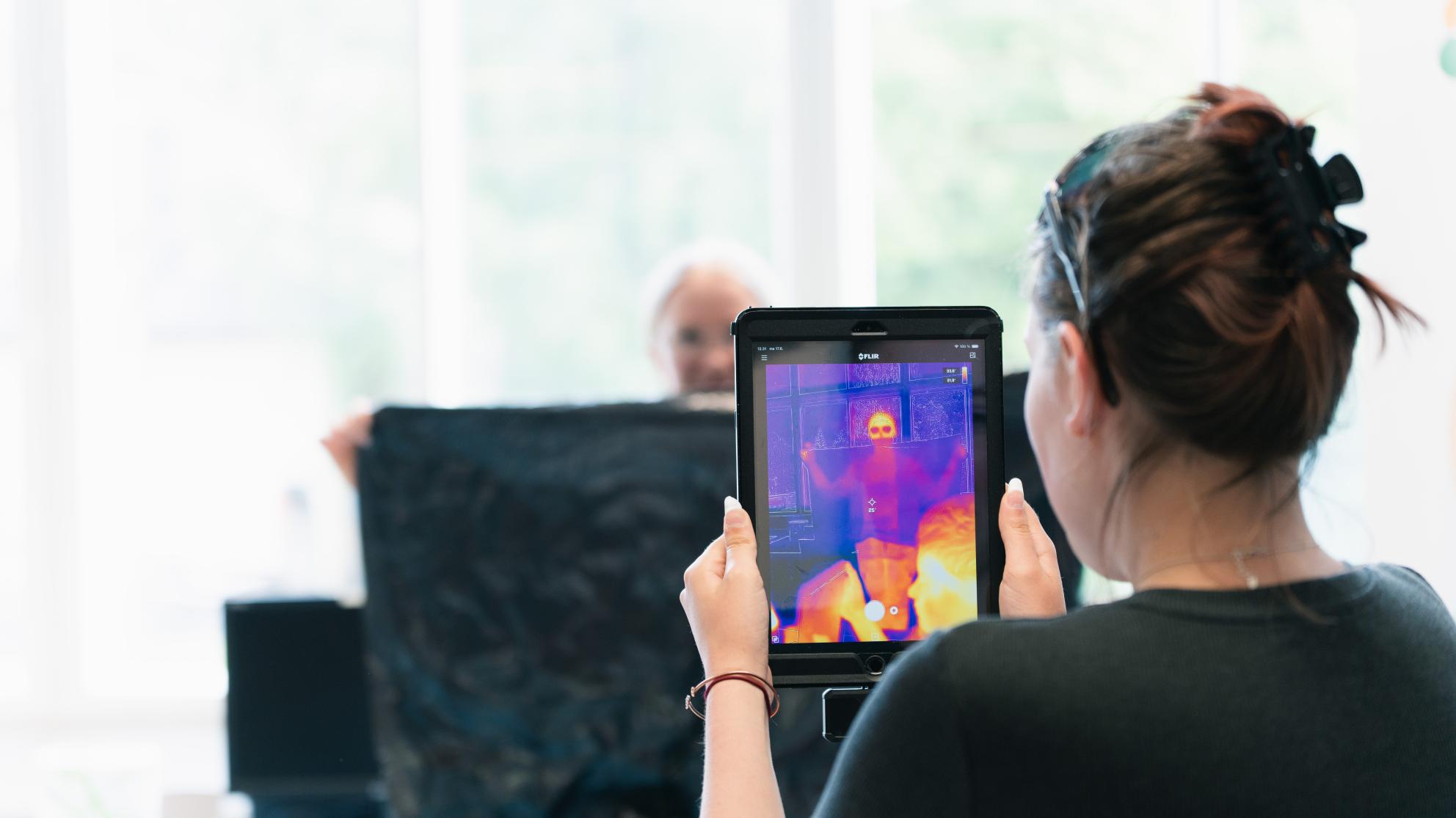 Tyttö kuvaa iPadissa kiinni olevalla lämpökameralla naista, joka seisoo jätesäkin takana.