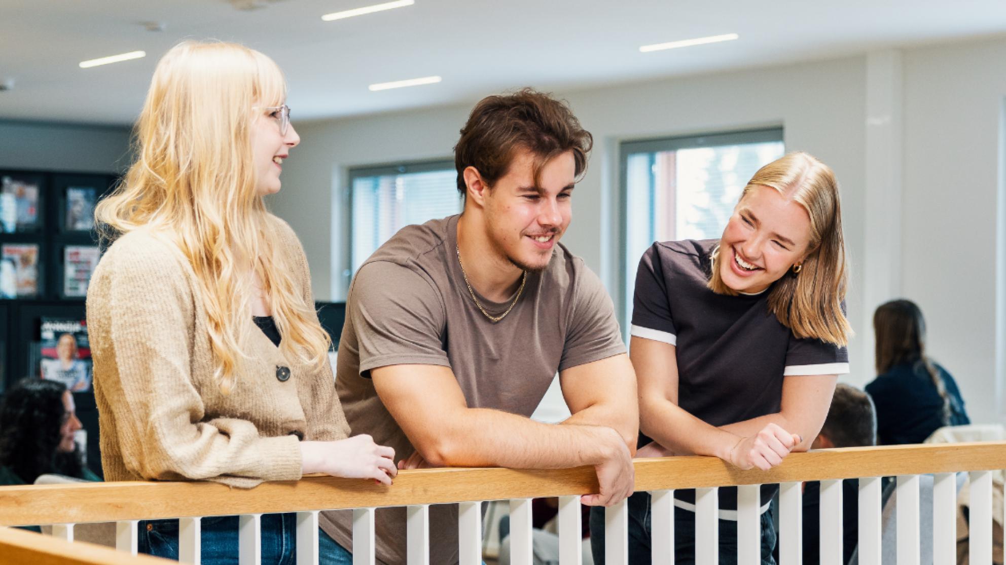 Kolme hymyilevää opiskelijaa nojaa porraskaiteeseen