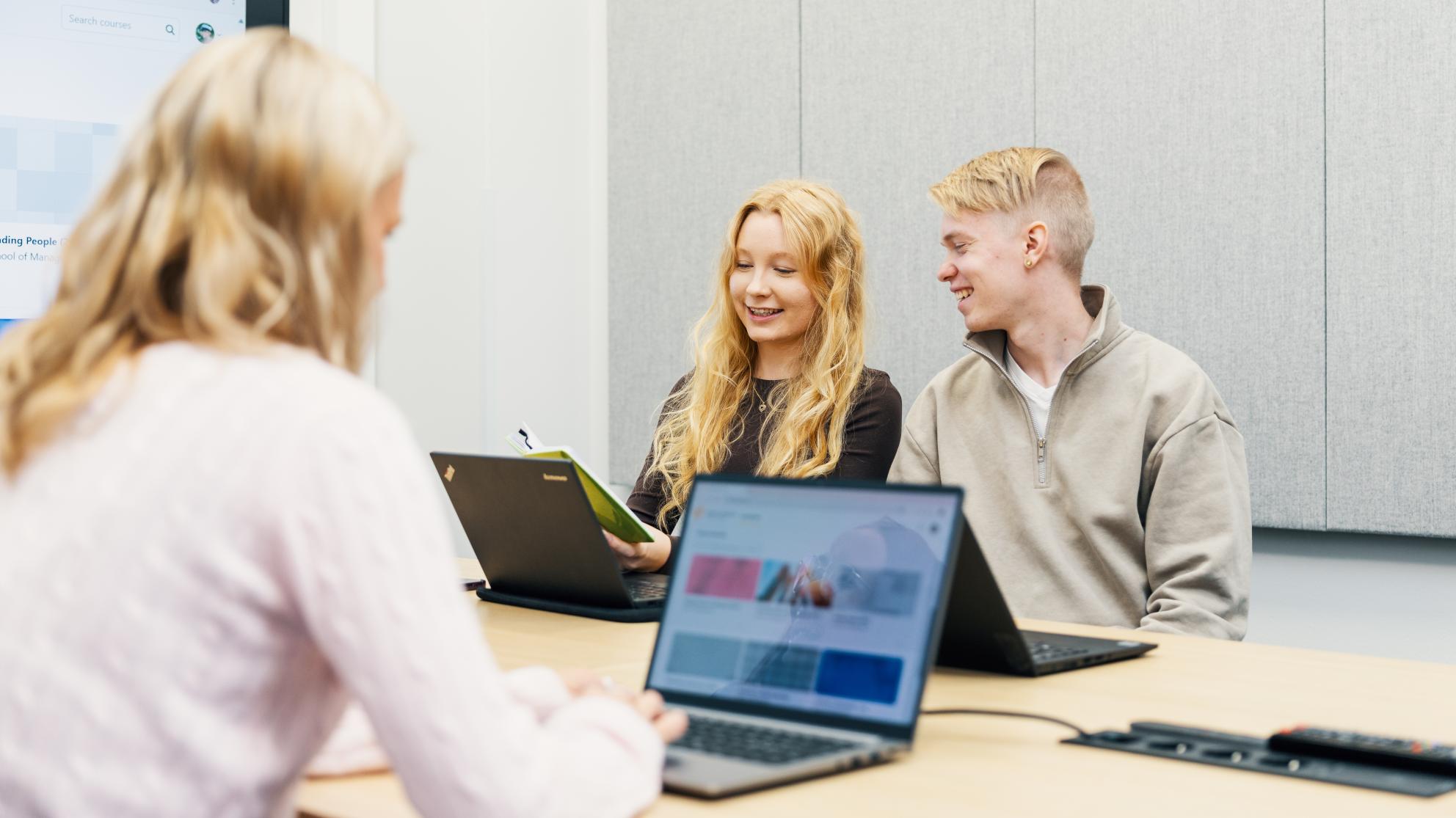 Kolme opiskelijaa pöydän ääressä tekemässä töitä tietokoneella.