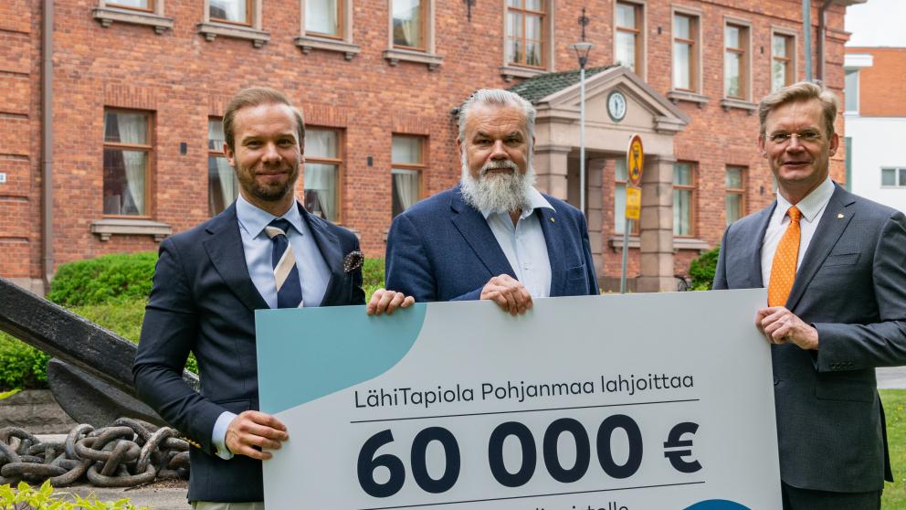 Kuva Joel Sunabackasta, Harry Linnarinteestä ja Jari Kuusistosta Konttorin edessä. He pitelevät 60000 euron lahjoituskylttiä käsissään.