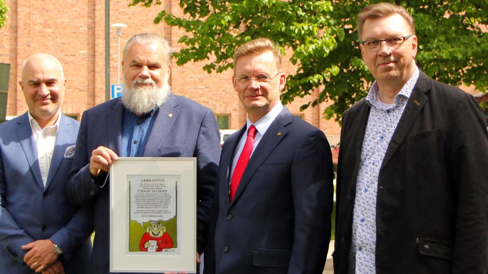 Alumnit rehtori ja yhteysjohtaja ulkona lahjakirjan kanssa