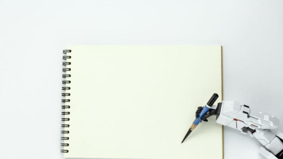 A robot hand is holding a pencil over a blank notebook