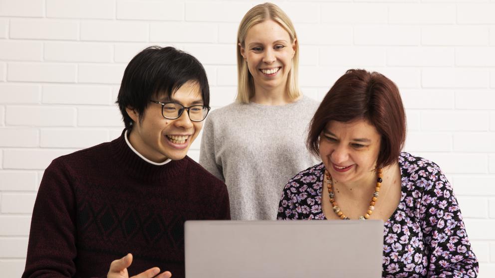 Three people looking at a laptop screen.