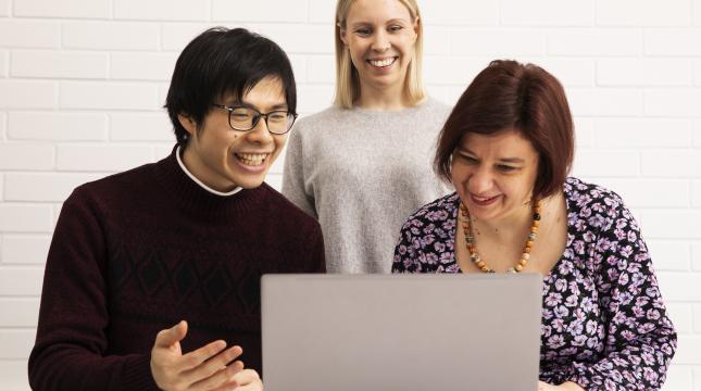 Three people looking at a laptop screen.