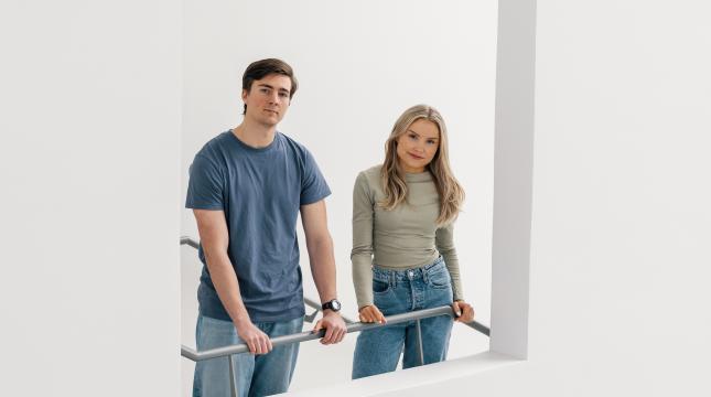 Tyttö ja poika katsovat kameraan porrastasanteella seisoen