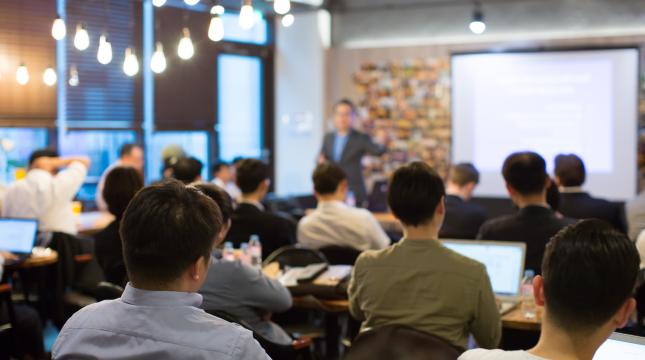 People gathered to watch a person giving a presentation in front. 