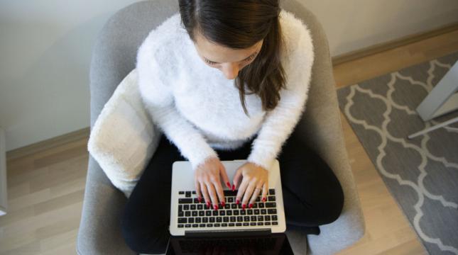 Nainen kirjoittaa nojatuolissa kannettavalla tietokoneella 