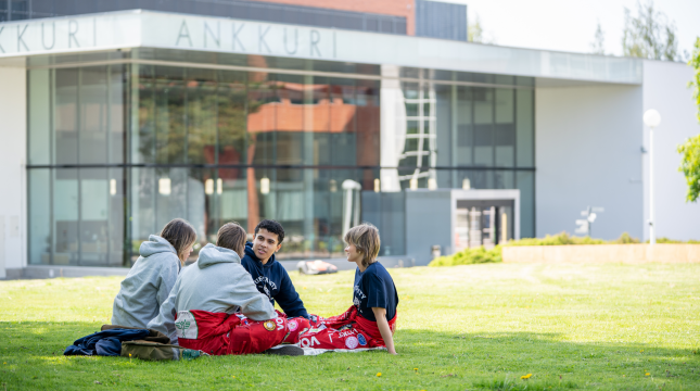 Opiskelijat istuvat nurmikolla kampuksella. 
