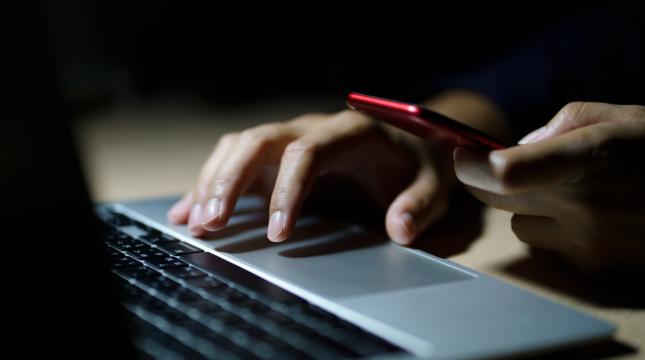 Ihminen näpyttelee kannettavaa tietokonetta toisessa kädessään matkapuhelin