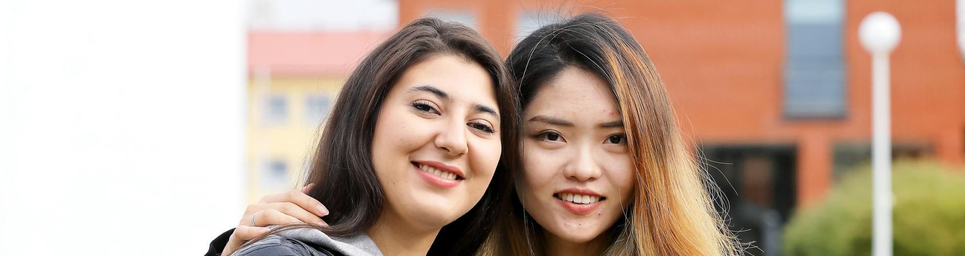 Kaksi opiskelijaa hymyilevät kameraan yliopiston kampuksella ulkona