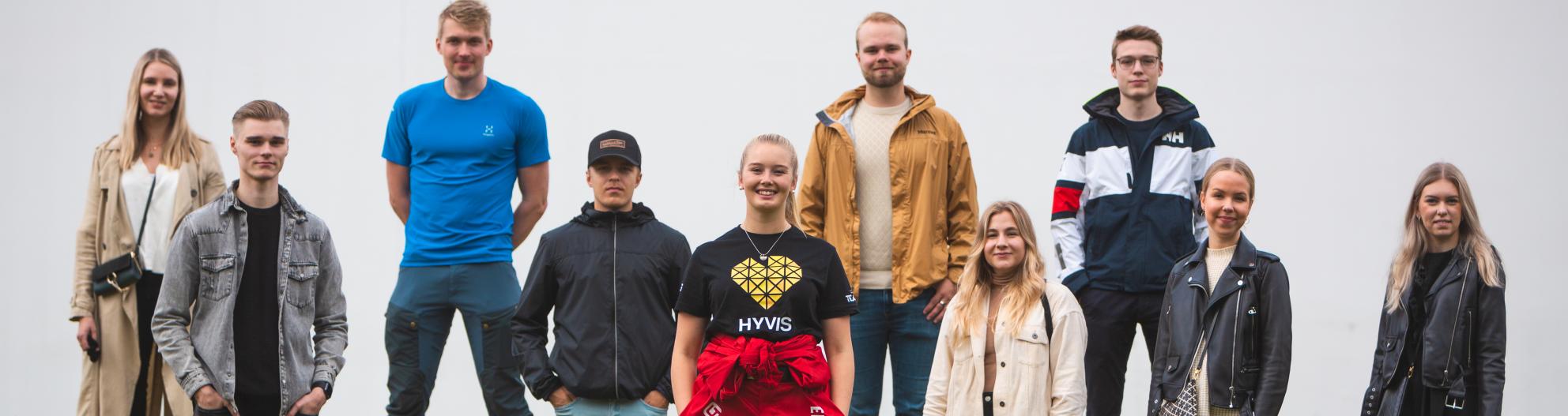 Opiskelijoita seisoo rivissä haalareihin pukeutuneen tuutorin takana