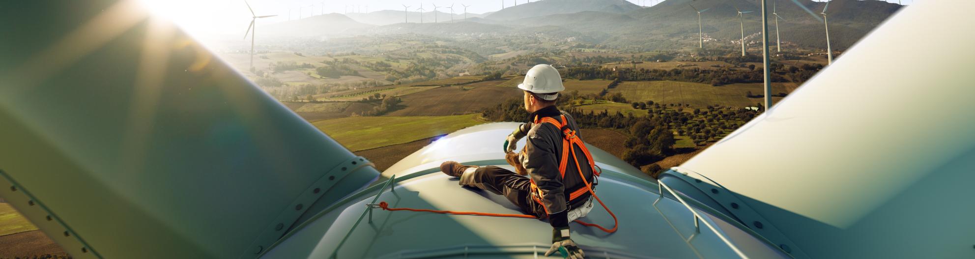 Worker sitting on the top of a wind turbine and looking at a sunny sky over a wind energy park