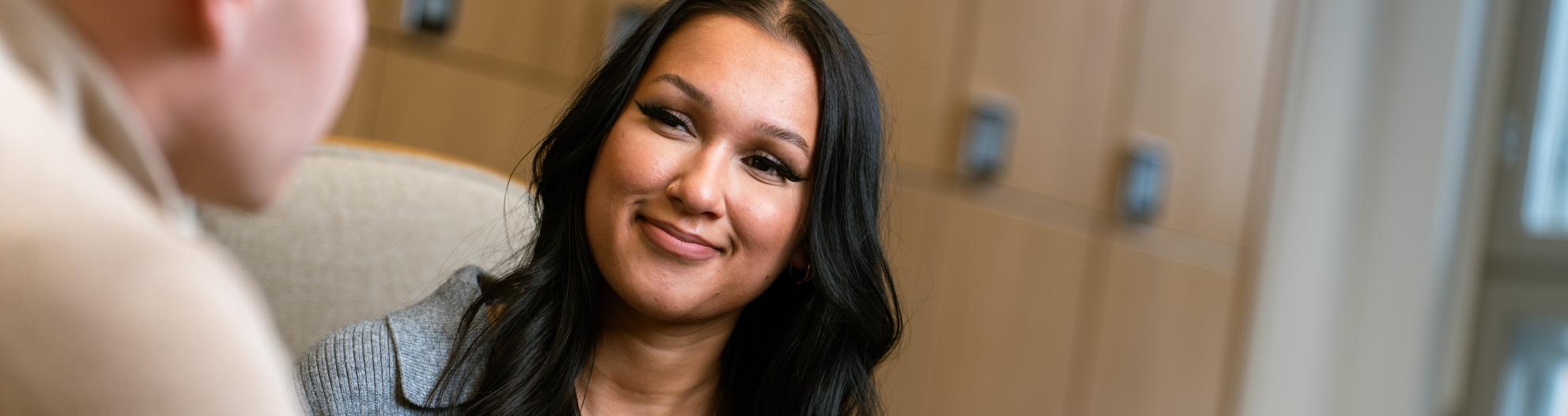 Kuvassa opiskelija hymyilee ja kirjoittaa muistiinpanoja