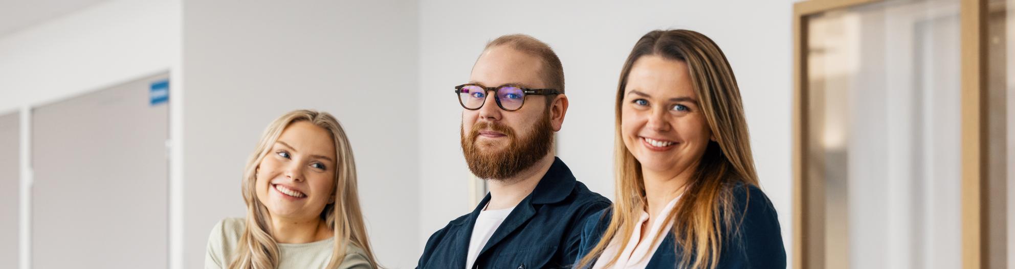  Opiskelijat hymyilevät kaiteseen nojaten ja katsovat kameraan