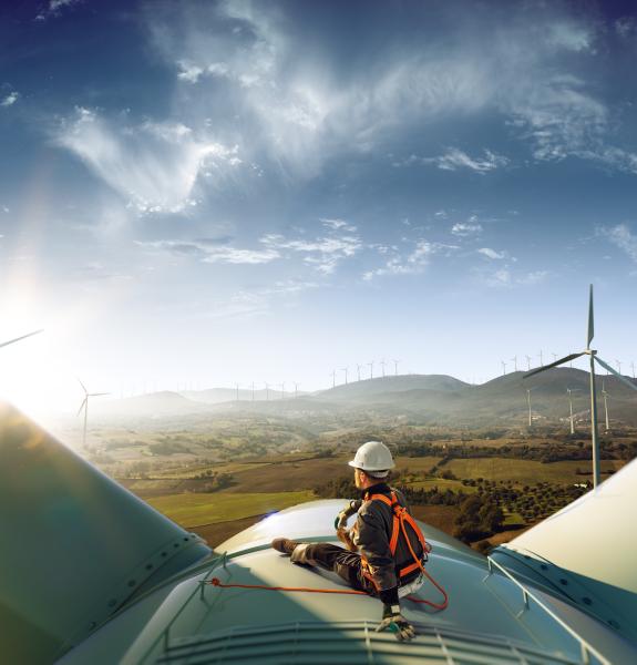 Worker sitting on the top of a wind turbine and looking at a sunny sky over a wind energy park