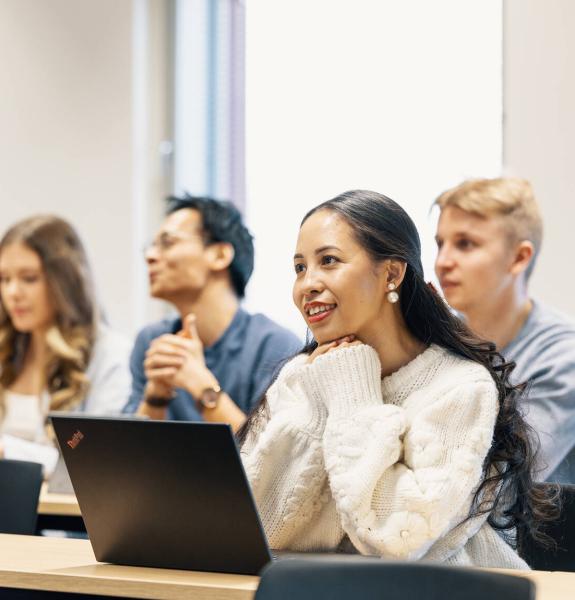 Opiskelijat luennolla ja nainen hymyilee etualalla