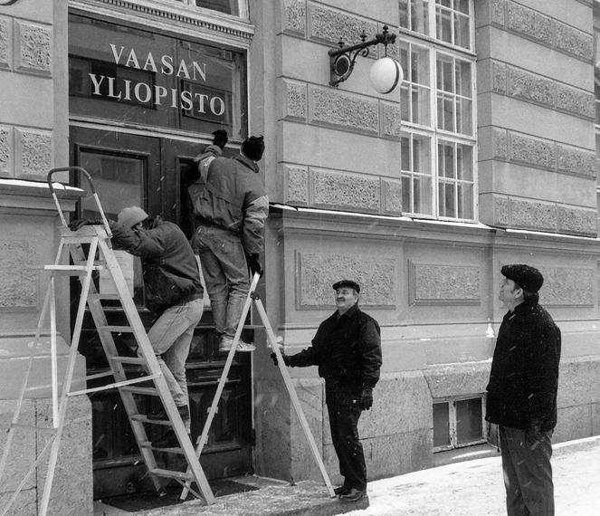 Nimikyltti vaihtuu. Rehtori Ilkka Virtanen oikealla, ylivirastomestari Tapio Silvennoinen pitää tikapuita Nimikyltti vaihtuu. Rehtori Ilkka Virtanen oikealla, ylivirastomestari Tapio Silvennoinen pitää tikapuita