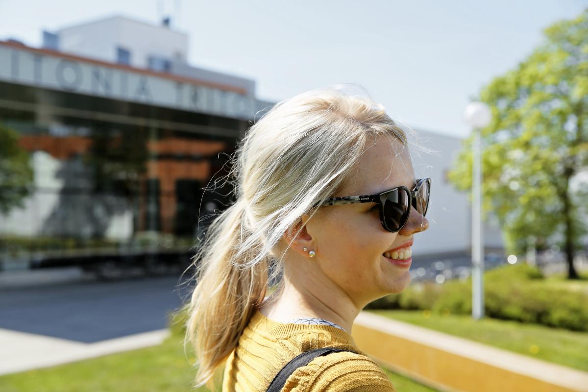 Opiskelija nauraa ulkona auringonpaisteessa yliopiston kampuksella. 