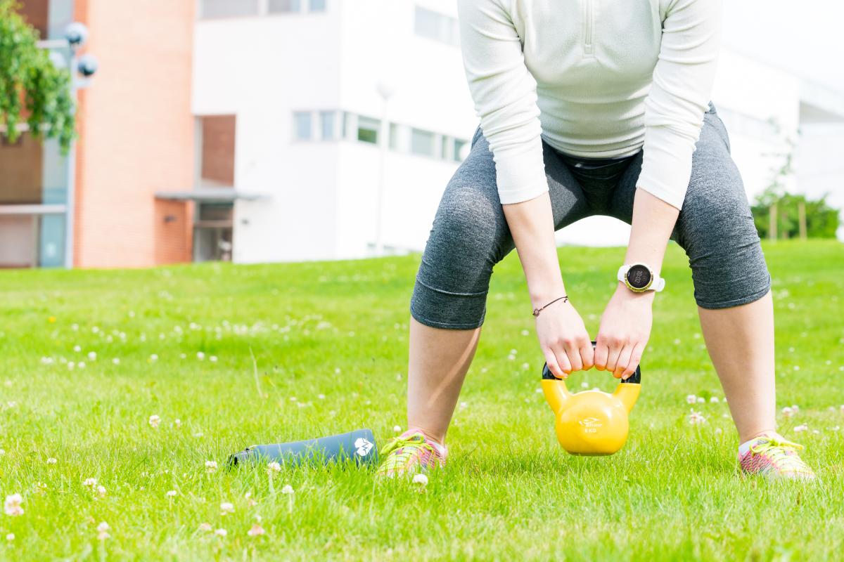 A close up of the campus lawn in the spring and a person working out with a kettlebell