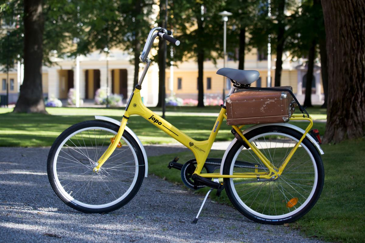A yellow bicycle with a piece of old luggage on the campus in the summer