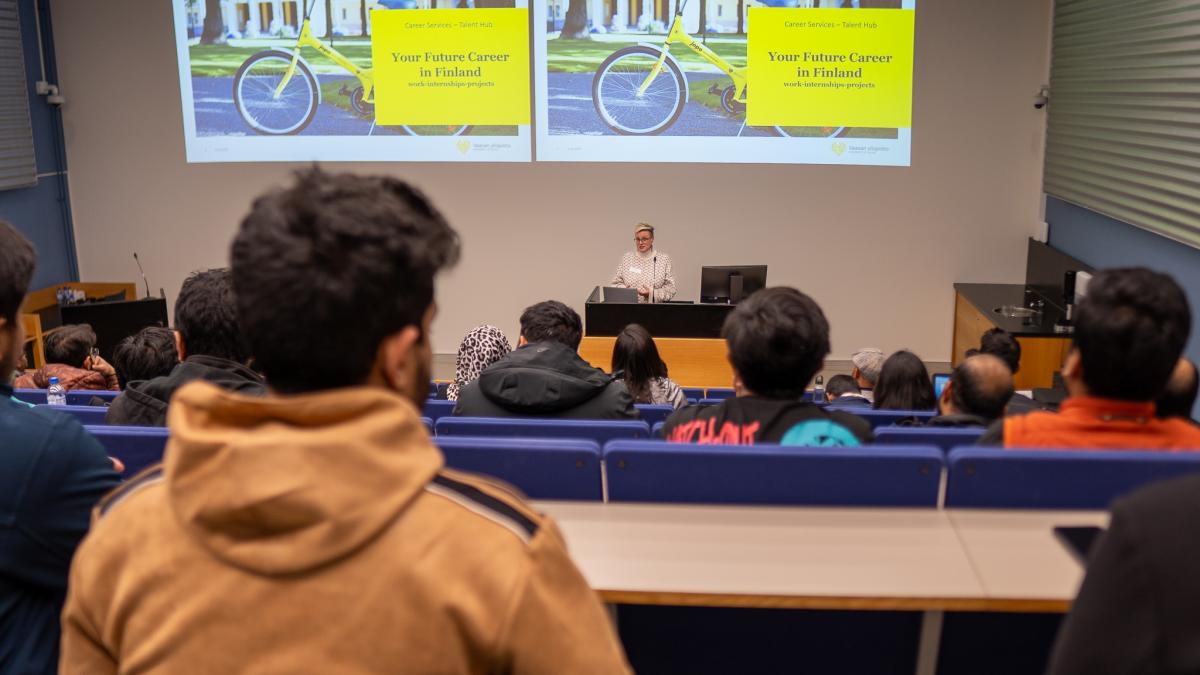 Hanna Turpeinen, Talent Hub Manager speaking to stodents. Text "Your Future Career in Finland" in the background. 