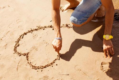 A hand shown drawing a heart in sand