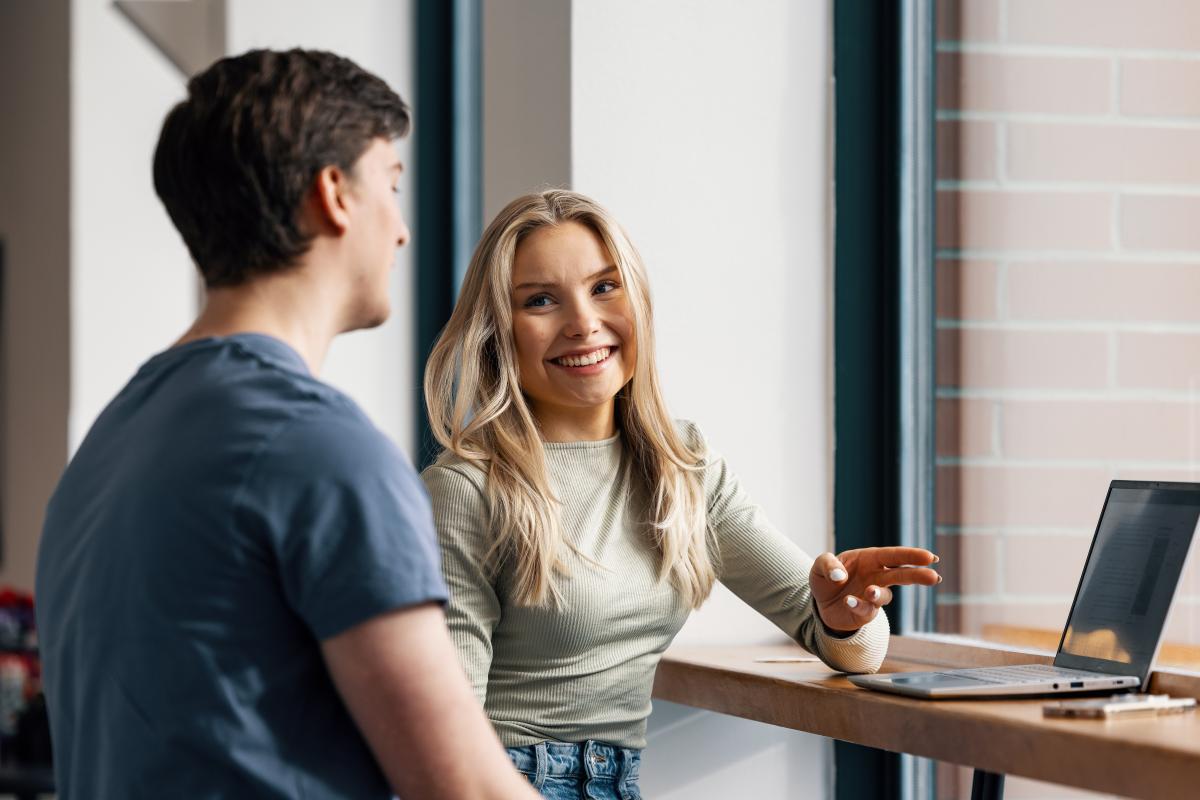 Hymyilevä tyttö osoittaa läppäriä ikkunan edessä