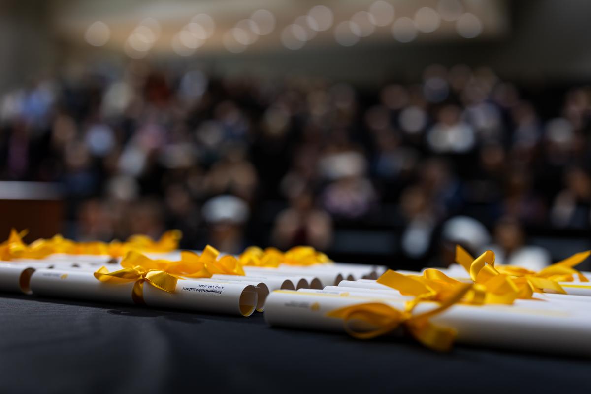 Muistamiskääröjä pöydällä valmiina jakamista varten. Taustalla näkyy sumeana auditorio täynnä ihmisiä.
