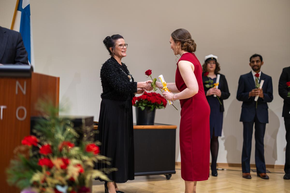 Rehtori Minna Martikainen ojentamassa ruusua valmistuneelle opiskelijalle.