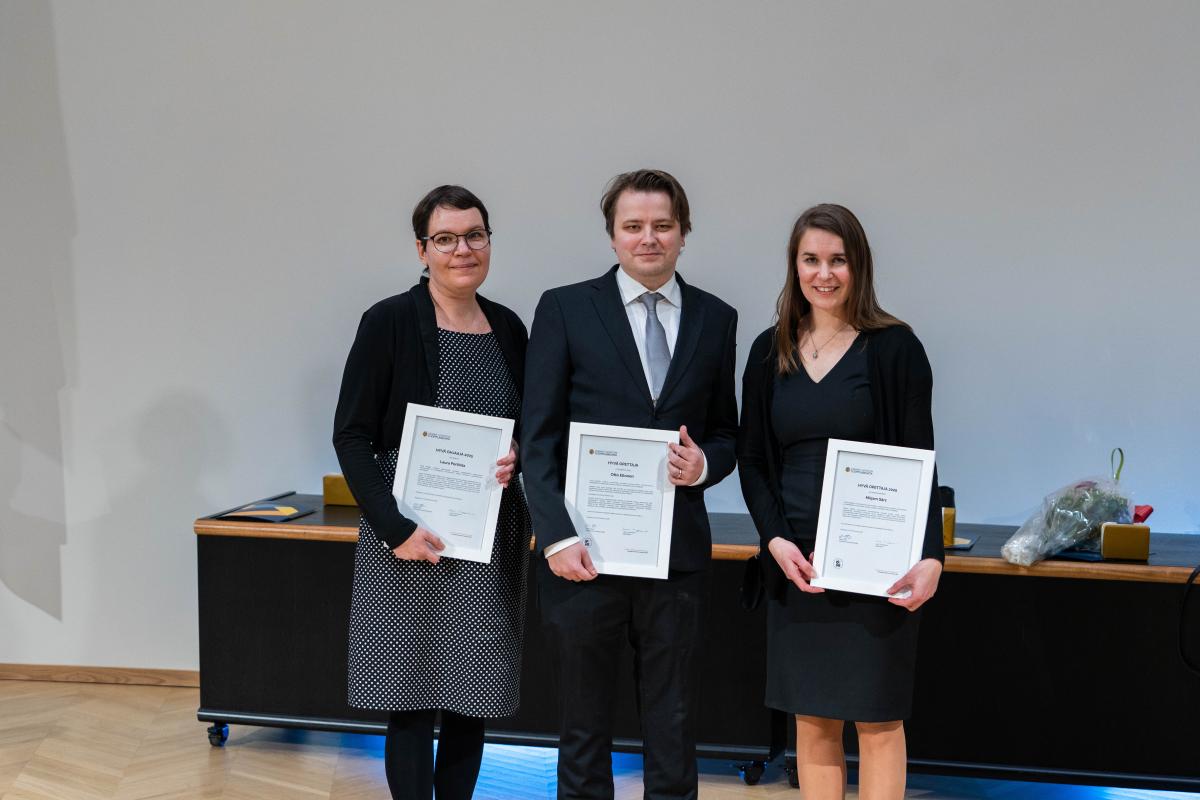 Kolme henkilöä seisomassa kunniakirjat käsissään. Jokainen katsoo kameraan ja hymyilee. Päällään heillä on juhlavaatteet.