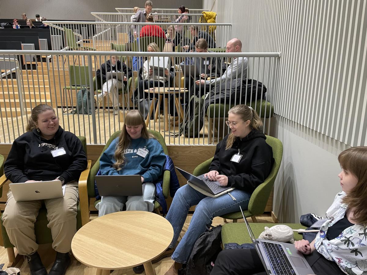 Opiskelijoita istumassa auditoriotilassa. He keskustelevat keskenään ja tekevät koulutehtäviä kannettavilla tietokoneilla.