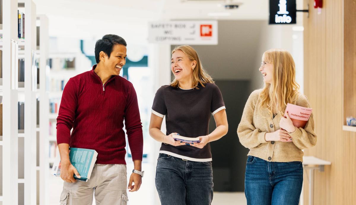 Kolme opiskelijaa kävelemässä kirjaston käytävällä