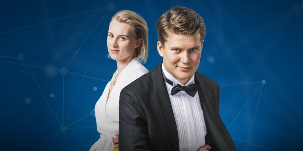 Kaksi henkilöä katsovat kameraan ja hymyilevät, sininen grafiikka taustalla