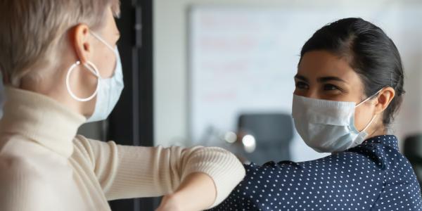 Two happy people greeting by touching elbows, with face masks on.