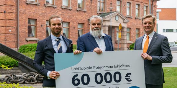 Kuva Joel Sunabackasta, Harry Linnarinteestä ja Jari Kuusistosta Konttorin edessä. He pitelevät 60000 euron lahjoituskylttiä käsissään.