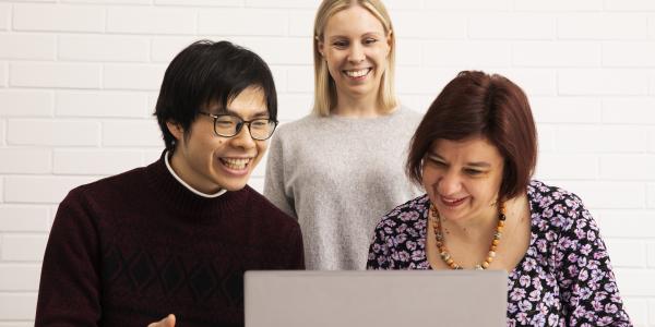 Three people looking at a laptop screen.